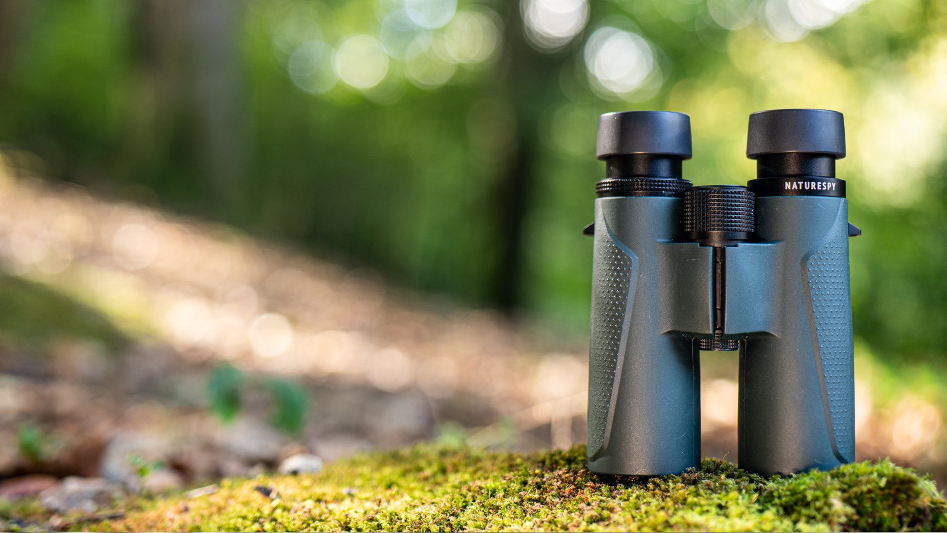 NatureSpy Tremarctos Binoculars on a grassy area with a blurred forest background